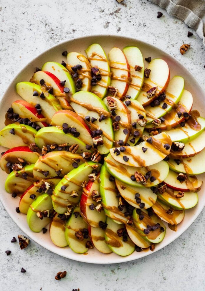 A large plate of apple nachos topped with a date caramel drizzle, mini chocolate chips, and pecans.